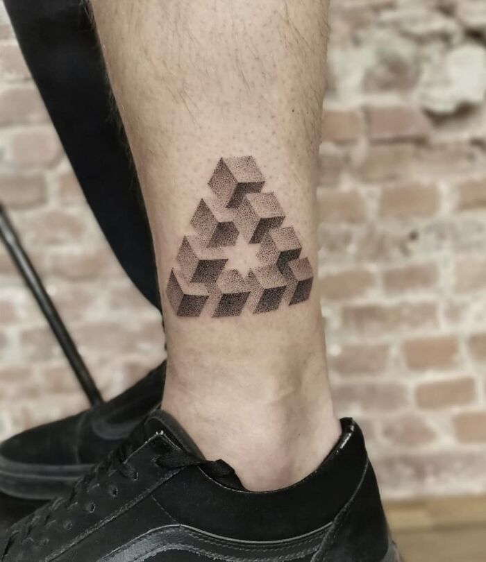 Optical illusion tattoo of an impossible triangle on a person's leg with geometric design.