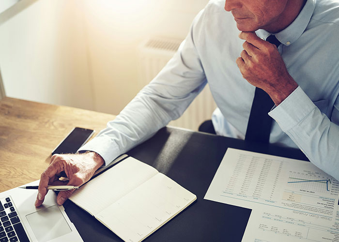 Man in office analyzing documents and laptop, considering reasons to sue.