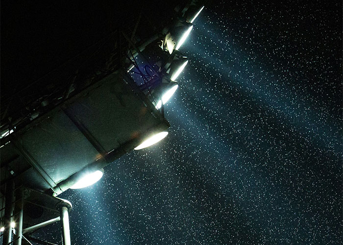 Floodlights illuminating falling rain at night, creating a dramatic scene.