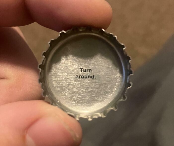 Close-up of a hand holding a bottle cap with the creepy message Turn around inside the cap.