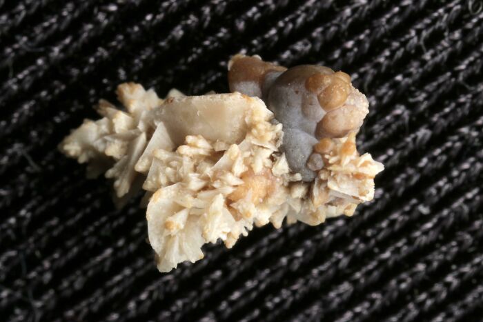 Close-up photo of a bizarre human body kidney stone with crystallized formations on a dark textured fabric background