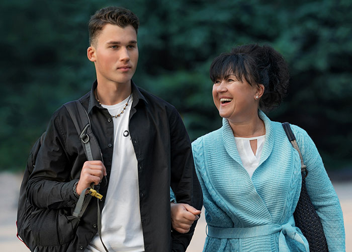 Teenager walking with his happy mother outdoors while stepmom throws tantrum after graduation invite decision.
