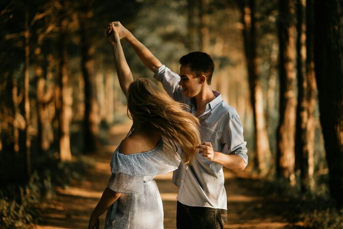 Couple dancing in a sunlit forest path, sharing a heartfelt and spicy moment away from others.