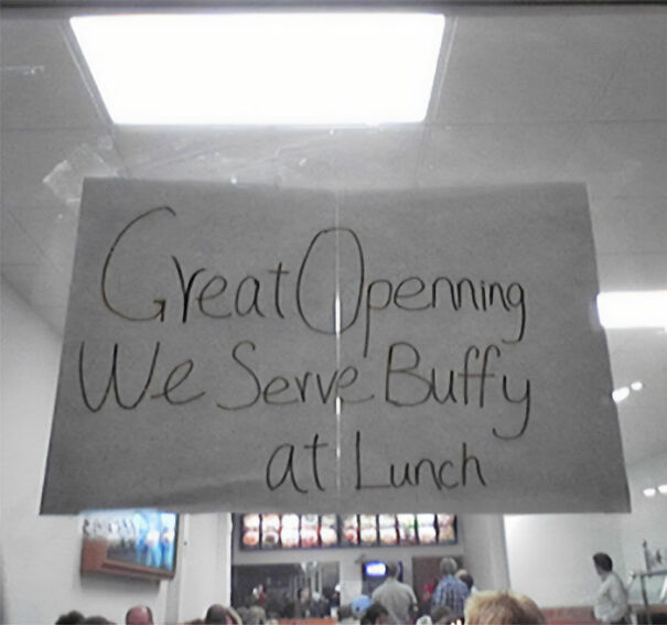 Handwritten sign with funny English use saying "Great Opening We Serve Buffy at Lunch" inside a busy restaurant setting.