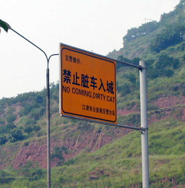 Road sign with a funny and baffling English translation reading no coming dirty cat against a hill background
